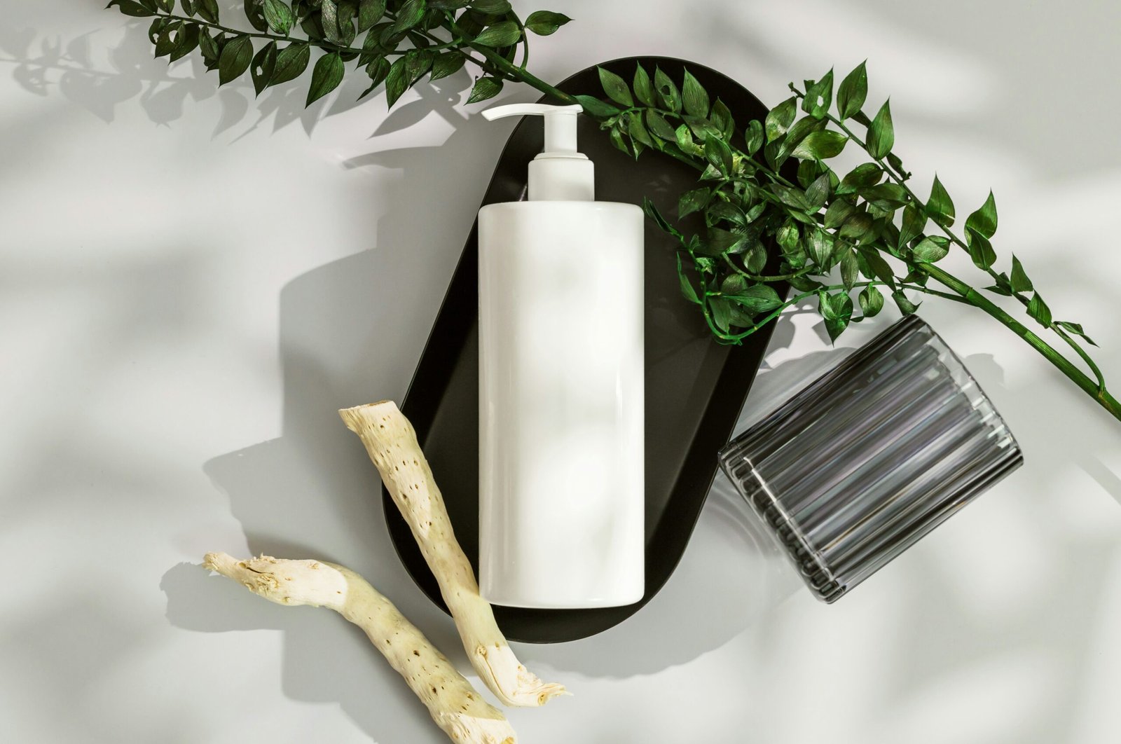 White shampoo bottle arranged on a black tray with green foliage and natural decorative elements in a minimalist setting.